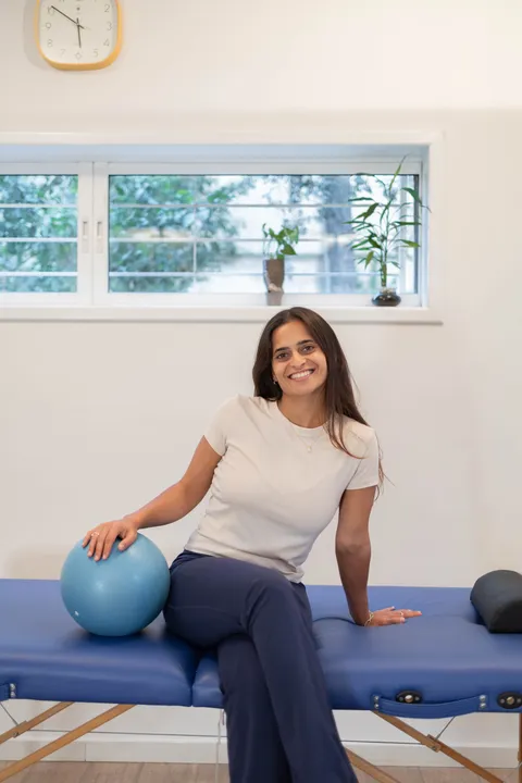 גל עופרי פיזיותרפיסטית מוסמכת יושבת על מיטת הטיפולים בקליניקה ומחייכת